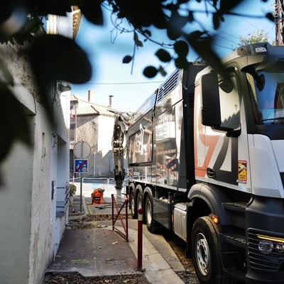 Excavatrice-aspiratrice en intervention urbaine avec un technicien de travaux publics sur une rue étroite.