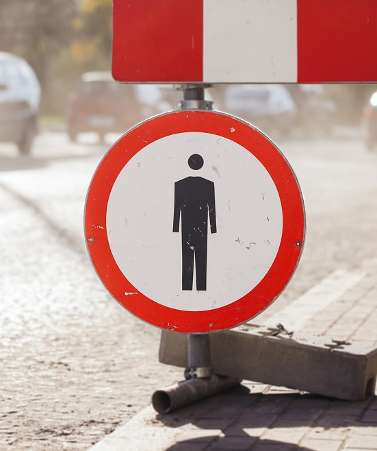 Panneau d'interdiction: silhouette d'homme sur route Panneau d'interdiction rouge et blanc montrant une silhouette d'homme noir, fixé près d'une barrière de travaux sur une route poussiéreuse.