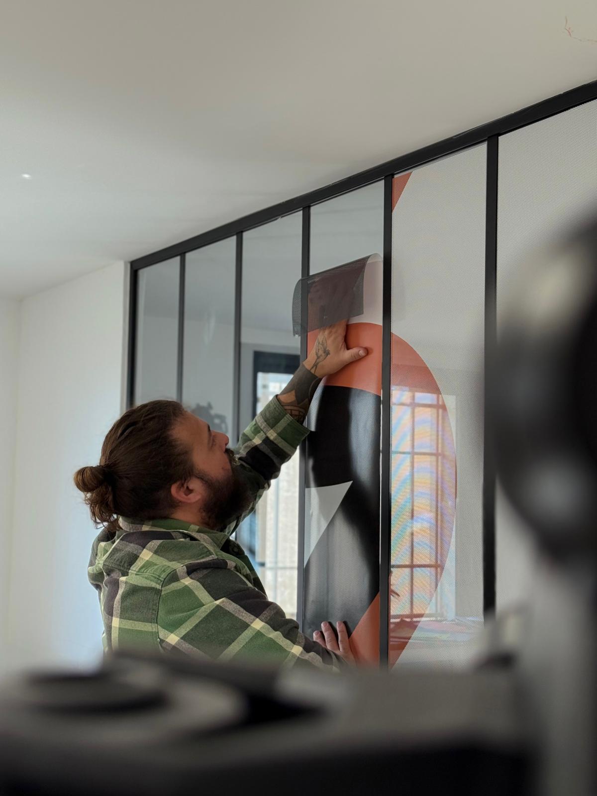 Pose de film adhésif décoratif sur cloison vitrée Pose d'un film adhésif décoratif sur une cloison vitrée à cadre noir par un professionnel minutieux.
