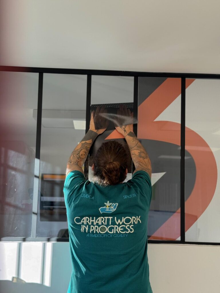 Pose de film adhésif et vitrophanie sur paroi vitrée Technicien tatoué posant un film sur vitrage en t-shirt Carhartt Work In Progress.