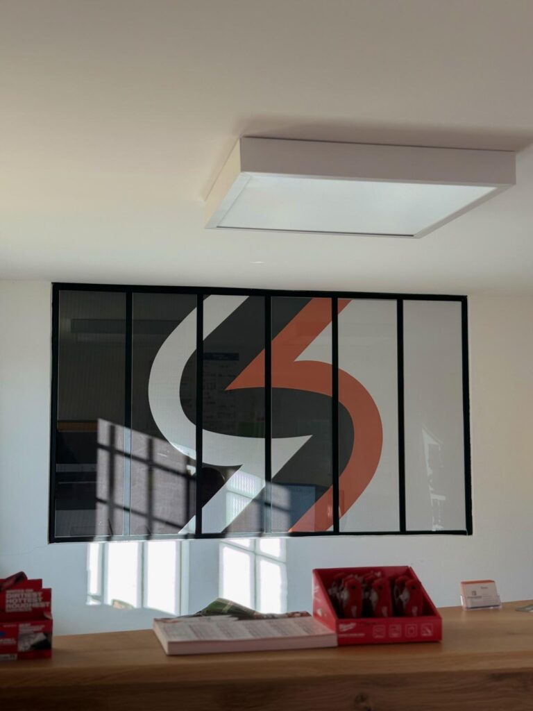 Décoration de Bureau : Logo Mural Moderne et Design Épuré Logo mural blanc et orange sur fond sombre dans un bureau moderne avec éclairage zénithal et ombres de fenêtres.