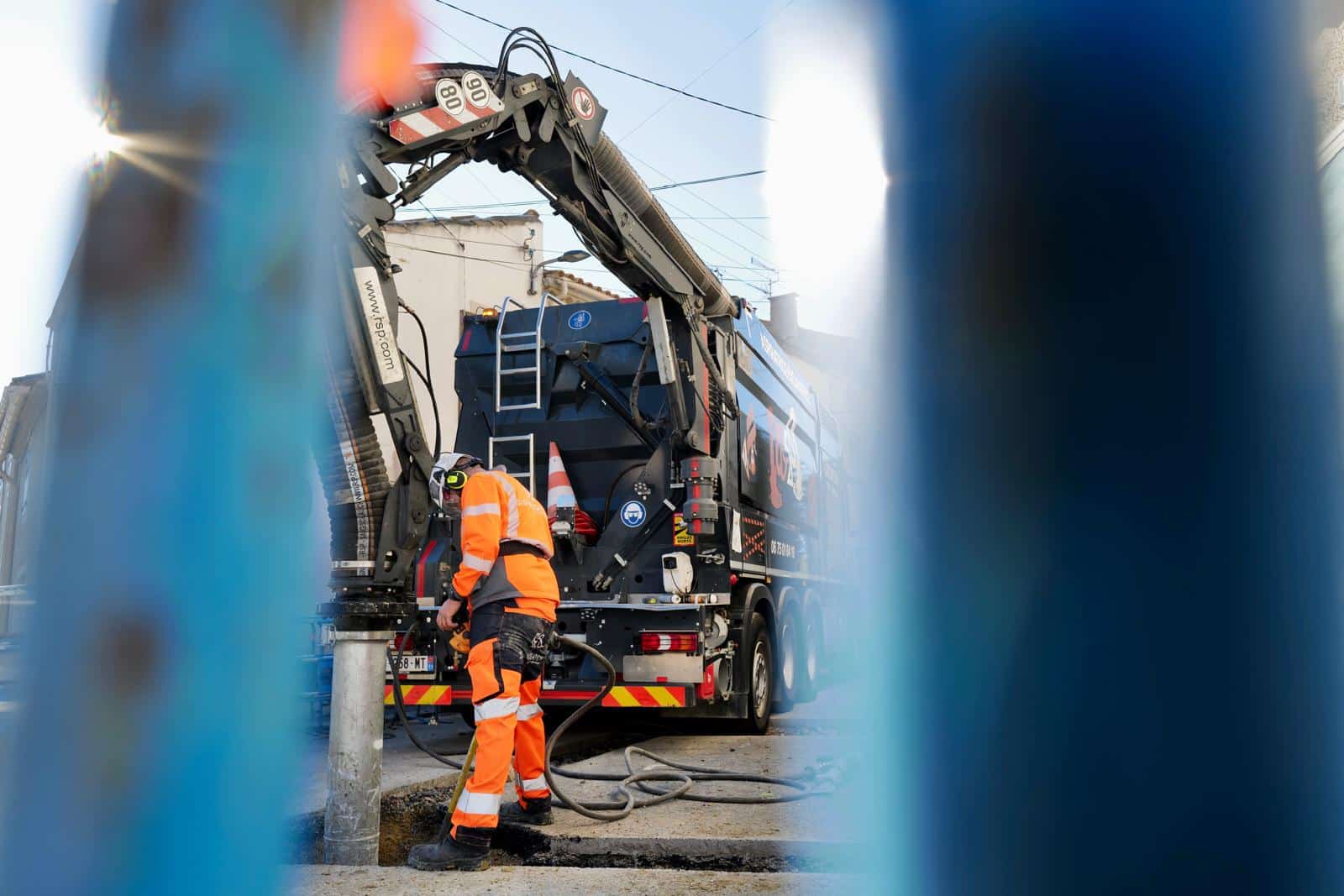 Travaux publics : aspiratrice excavatrice RSP sur chantier Ouvrier en tenue orange utilisant une aspiratrice excavatrice RSP sur un chantier de voirie avec tuyau d'aspiration.