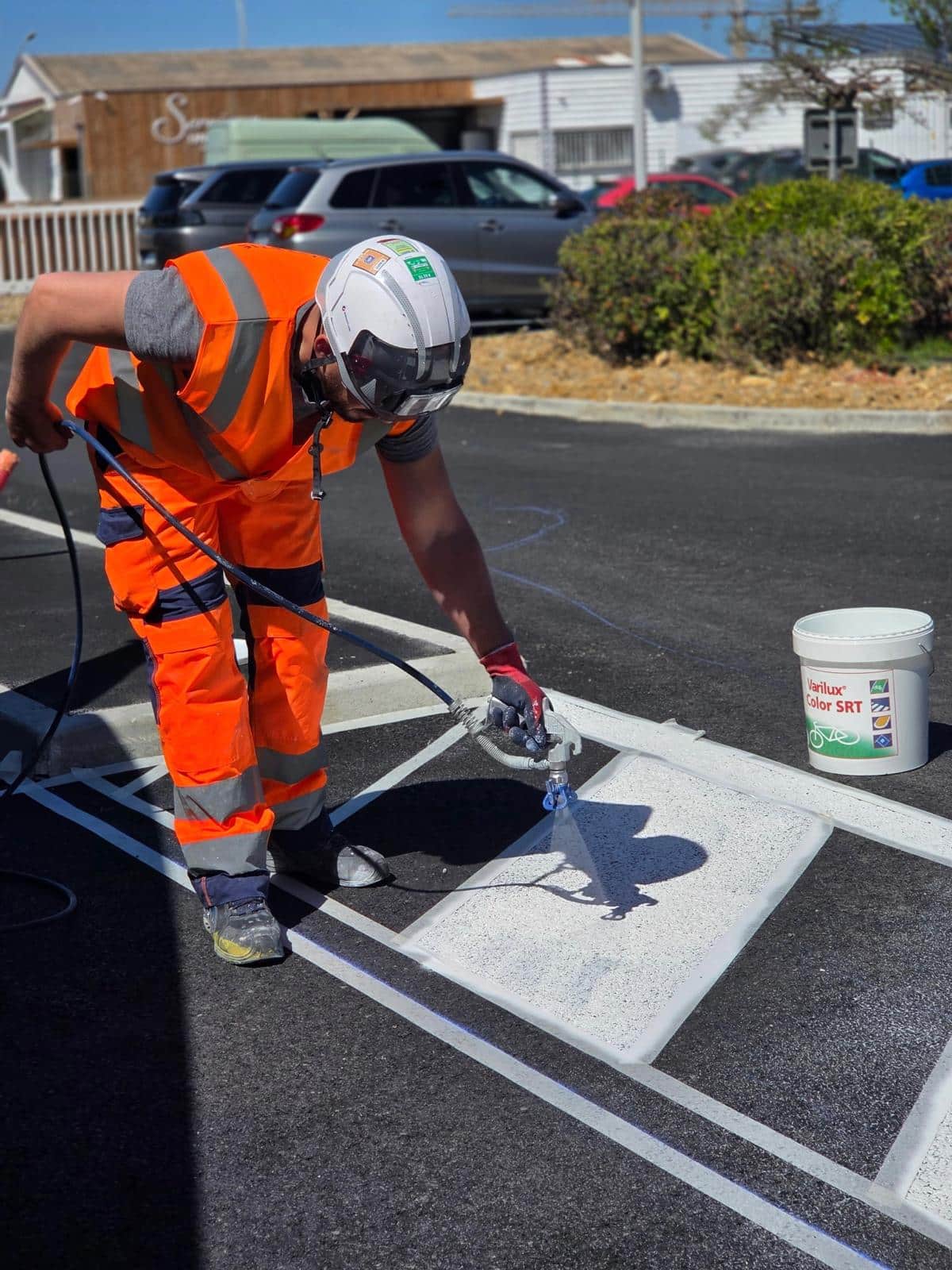 Marquage au sol routier avec peinture Varilux Color SRT Marquage au sol à la peinture blanche Varilux Color SRT par un ouvrier en tenue de sécurité orange.