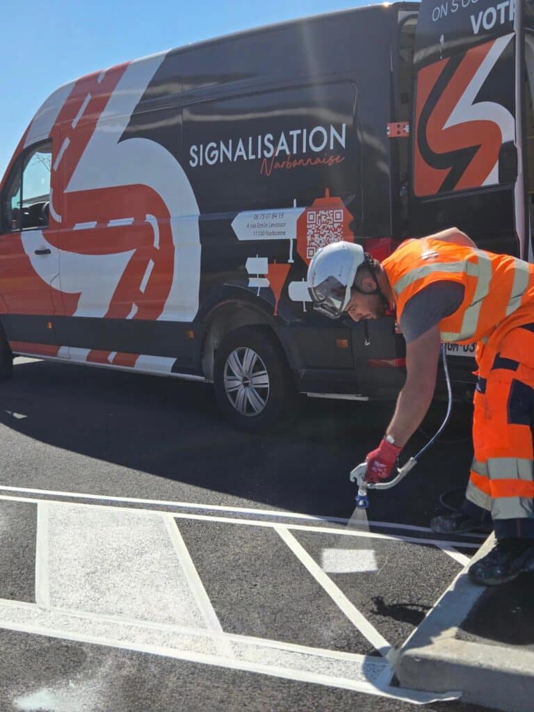 Employé de Signalisation Narbonnaise traçant des lignes de marquage au sol avec un pistolet pulvérisateur.